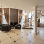 Interior of spacious hallway of classic styled villa with columns and comfortable leather sofa and armchair placed near spiral staircase